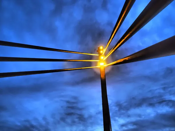 Holofotes na ponte. Torre de luz LED portátil. Ponte pedestre de Santo Irineu sobre o rio Sava, Sremska Mitrovica, Sérvia. Noite céu azul com nuvens. Pilares e vigas de metal, perspectiva — Fotografia de Stock