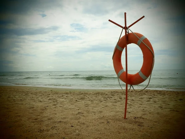 Lifebuoy on a sandy beach. Orange circle on a pole to rescue people drowning in the sea. Rescue point on the shore. Sky and sea in the background. Dark vignetting around the edges.