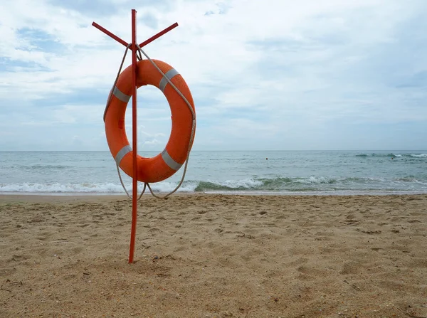 Lifebuoy on a sandy beach. Orange circle on a pole to rescue people drowning in the sea. Rescue point on the shore. Sky and sea in the background.