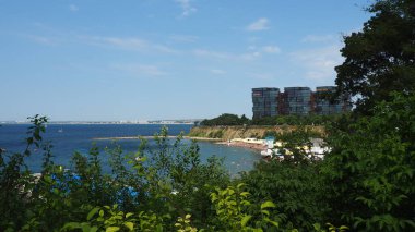 Anapa, Rusya, 23 Ağustos 2021 Vysokiy Bereg plajı, çalılıklardan manzara. Turistler yüzer ve güneşlenir. Yaz günü. Denizde tatil ve turizm. Modern çok katlı binalar. Mavi gökyüzü ve deniz, ufuk.