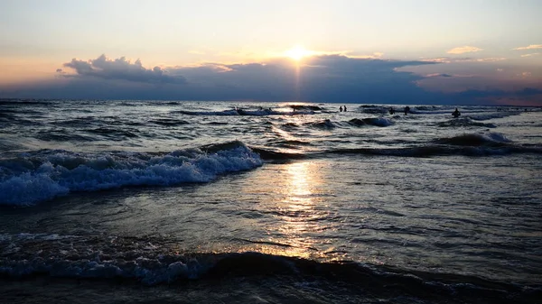 Olas con espuma. Hermoso atardecer. Olas espumosas rodan sobre la orilla arenosa. Vityazevo, Anapa, Mar Negro. Meca turística, centro de salud. Nubes coloridas en el cielo de la tarde. Los rayos se reflejan en el agua — Foto de Stock