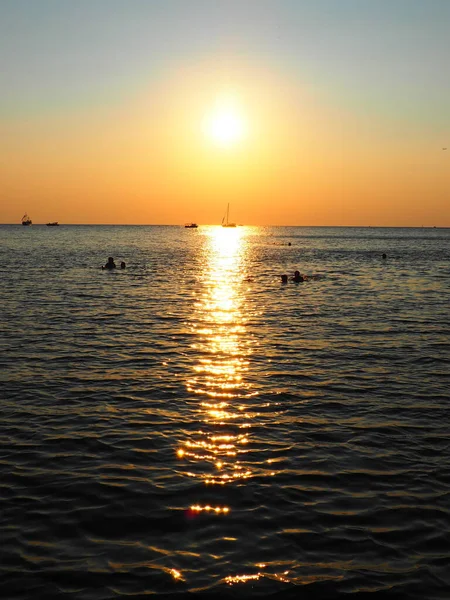 Anapa, Rusia 23 Agosto 2021 Puesta de sol sobre el mar. Hermosas olas al atardecer. Meca turística, resort. Cielo nocturno. Los rayos se reflejan en el agua. Naves y personas nadando en el mar — Foto de Stock