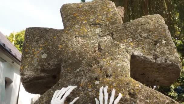 Σκελετός χέρια ζόμπι αυξάνεται από ένα νεκροταφείο, Απόκριες. Τα οστά των χεριών του σκελετού στην ταφόπλακα. Ο νεκρός που ζωντάνεψε. Παλαιοχριστιανικό νεκροταφείο και πέτρα βρύα σταυρό — Αρχείο Βίντεο
