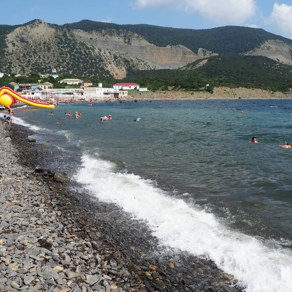 Sukko, Russland 25. August 2021 Felsstrand mit Wellen, Anapa. Meerschaum auf einem Kieselstrand. Große runde Kieselsteine und Felsbrocken im Wasser. Schwarzes Meer, Kaukasus. Touristen schwimmen und genießen. Menschen sonnen sich — Stockfoto