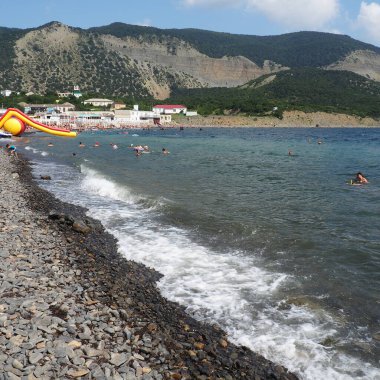 Sukko, Rusya 25 Ağustos 2021 dalgalı kayalık plaj, Anapa. Çakıl taşlı sahilde deniz köpüğü. Suda büyük yuvarlak çakıl ve kaya parçaları var. Karadeniz, Kafkaslar. Turistler yüzer ve eğlenir. İnsanlar güneşleniyor.