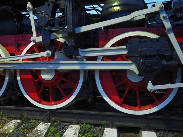 Retro vintage wheels of a locomotive or train close up. Red large heavy metal wheels with piston guiding mechanisms. Locomotive of the 19th - 20th centuries with a steam engine. — Stock Photo, Image