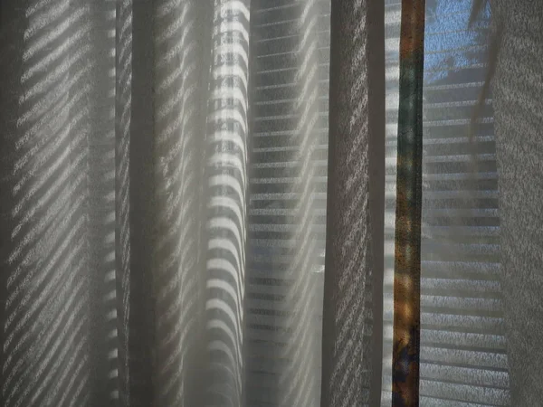 タルとブラインドが窓に。光カーテン太陽のまぶしさと光線で透明な布。目が覚めた後の晴れた朝。リビングルームの内部にオフィスブラインド。内部のプライバシー — ストック写真