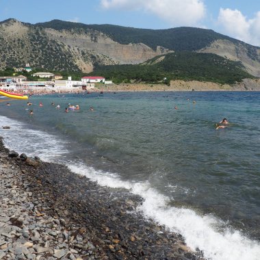 Sukko, Rusya 25 Ağustos 2021 dalgalı kayalık plaj, Anapa. Çakıl taşlı sahilde deniz köpüğü. Suda büyük yuvarlak çakıl ve kaya parçaları var. Karadeniz, Kafkaslar. Turistler yüzer ve eğlenir. İnsanlar güneşleniyor.