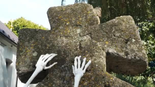 Manos de zombi esqueleto saliendo de un cementerio, Halloween. Los huesos de las manos del esqueleto en la lápida. El hombre muerto que ha cobrado vida. Antiguo cementerio cristiano y cruz de musgo de piedra — Vídeos de Stock