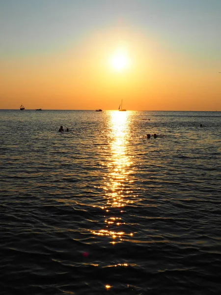 Anapa, Rusia 23 Agosto 2021 Puesta de sol sobre el mar. Hermosas olas al atardecer. Meca turística, resort. Cielo nocturno. Los rayos se reflejan en el agua. Naves y personas nadando en el mar —  Fotos de Stock