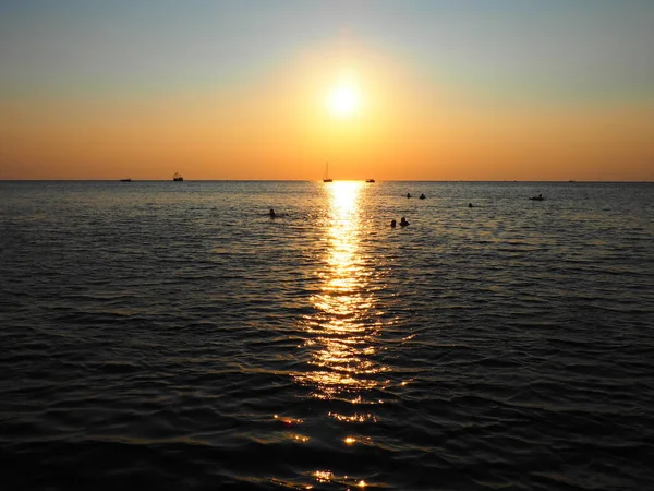 Anapa, Rusia 23 Agosto 2021 Puesta de sol sobre el mar. Hermosas olas al atardecer. Meca turística, resort. Cielo nocturno. Los rayos se reflejan en el agua. Naves y personas nadando en el mar — Foto de Stock