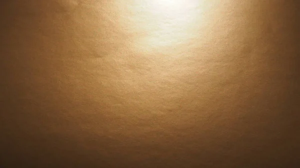 Gelb-braunes Papier mit metallischem Glanz, die Beleuchtung leuchtet von oben. Abstrakter Hintergrund mit Farbverlauf. Kopierraum. Textur und Unebenheiten auf der Oberfläche. Der Glanz einzelner Punkte. — Stockfoto