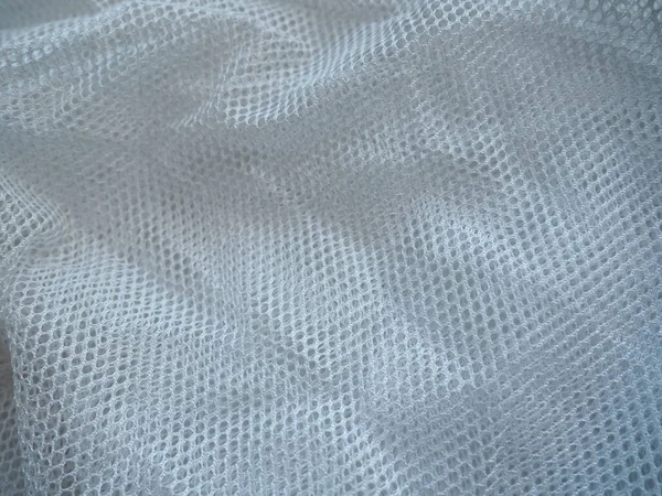 Sheer white net-like tulle. Mesh fabric is wrinkled or folded carelessly. Close-up. White - blue veil or muslin