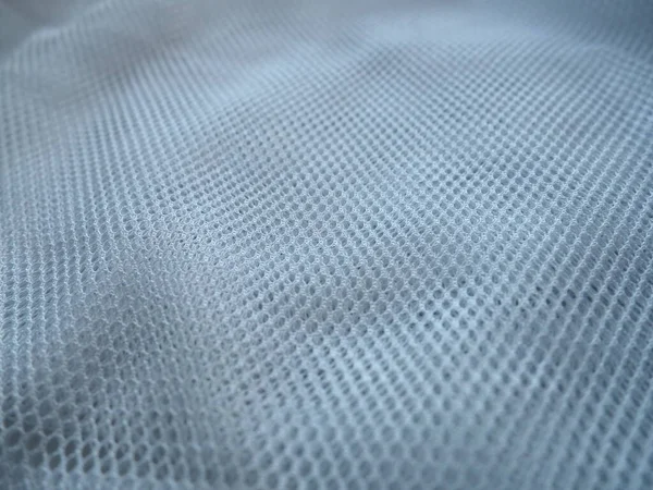 Sheer white net-like tulle. Mesh fabric is wrinkled or folded carelessly. Close-up. White veil or muslin. Curtain with holes of different sizes close-up