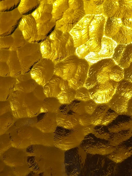 Vidro ondulado amarelo dourado com um fundo claro e escuro. reflexões de luz. Vidro ondulado, fonte de luz traseira. Jogo de brilho e reflexões em uma superfície irregular transparente. — Fotografia de Stock