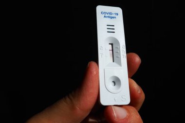 COVID-19 için test sonuçları net değil, hızlı test ekipmanları kullanılıyor. Elinde koronavirüs testi, siyah arka plan. Uzayı kopyala Bir şerit ve hamura bulaşmış bölge. Belirsiz tanı.