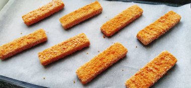 Donmuş balık çubukları kağıt üzerine serilmiştir. Balık lezzeti pişiriyorum. Pişirme tepsisinde kağıt yapmak. Fırından hızlı bir öğle yemeği. Balık menüsü. Sağlıklı protein yiyeceği. Düşük kalorili diyet.