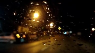 Gece araba sürüyorum. Arabanın ön camında yağmur damlaları var. Asfalt yolu ya da patika. Bulanık ve odaksız etki. Camdaki damlacıklara odaklan. Park halindeki arabalar ve gece ışıkları Sırbistan Sremska Mitrovica
