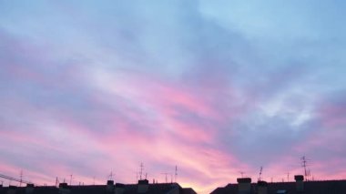 Akşam gökyüzü ve pembe bulutlar. Şehir binalarının üzerinde gün batımı. Zaman atlamalı bir atmosferde hızlandırılmış hareket. Güzel bulutlar. Gökyüzünde hızlı hareket eden bulutlar. Yavaş yavaş kararma