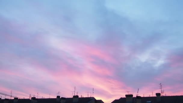 夕方の空とピンクの雲 街の建物の上に夕日 時間経過の雰囲気の中で加速運動 綺麗な雲だ 空を渡る雲の急速な動き 徐々に暗くなる — ストック動画