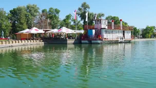 Palich lake, Serbia, 09.11.2021.白天，水库岸边的咖啡店和餐馆。船务餐厅与游客同行的愉快船。人们都在放松。水面上的波纹。桑尼. — 图库视频影像