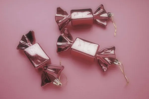 以糖果为形式的圣诞装饰 三只包装在和平粉色背景下的糖果 新年和圣诞节漂亮的装饰品 挂的线 粉色背景 模糊的重点 — 图库照片