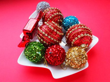 Noel ağacı şeklinde beyaz bir tabakta çok renkli Noel topları ve şekerler. Kırmızı pembe arka plan. Güzel çizgili kırmızı, pembe, yeşil, gümüş, sarı, mavi, altın Noel süslemeleri