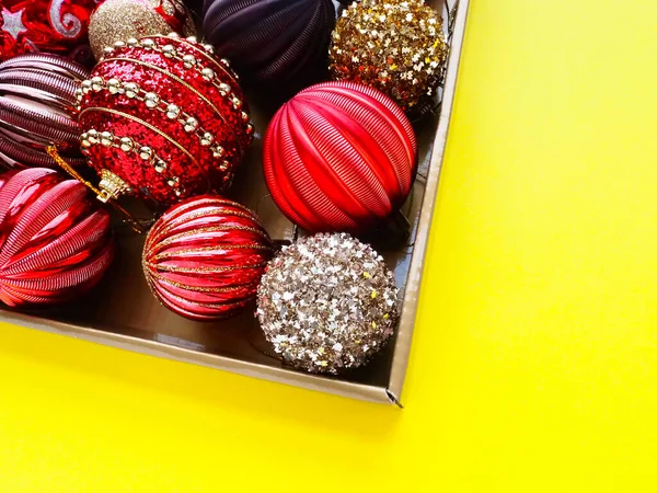 Dekoracje Świąteczne Pudełku Żółtym Tle Piękne Czerwone Złote Kulki Błyszczącymi — Zdjęcie stockowe