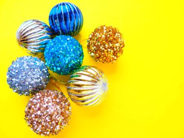 Sarı arka planda Noel süsleri. Parlak ve çizgili güzel mavi, gümüş ve altın toplar. Yılbaşı tatiline hazırlanıyorum. Güzel parlak dekorasyonlar. Boşluğu kopyala