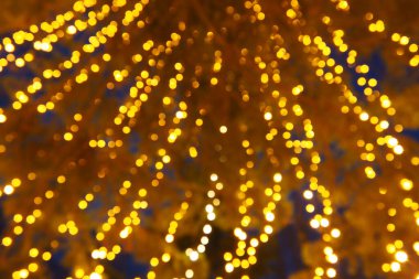 Bokeh röfleleri. Karanlıkta sarı ve altın rengi yanıp sönüyor. Şenlik arka planı. Bulanık defocus. Şehir sokaklarının dekorasyonu. Bir sürü sarı top. Birçok sarı, beyaz ve turuncu daireler