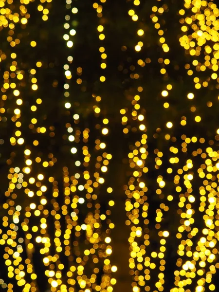Bokeh röfleleri. Karanlıkta sarı ve altın rengi yanıp sönüyor. Şenlik arka planı. Bulanık defocus. Şehir sokaklarının dekorasyonu. Bir sürü sarı top. Birçok sarı, beyaz ve turuncu daireler