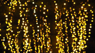 Bokeh röfleleri. Karanlıkta sarı ve altın rengi yanıp sönüyor. Şenlik arka planı. Bulanık defocus. Şehir sokaklarının dekorasyonu. Bir sürü sarı top. Birçok sarı, beyaz ve turuncu daireler