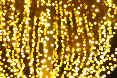Bokeh röfleleri. Karanlıkta sarı ve altın rengi yanıp sönüyor. Şenlik arka planı. Bulanık defocus. Şehir sokaklarının dekorasyonu. Bir sürü sarı top. Birçok sarı, beyaz ve turuncu daireler
