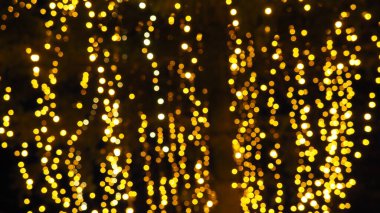 Bokeh röfleleri. Karanlıkta sarı ve altın rengi yanıp sönüyor. Şenlik arka planı. Bulanık defocus. Şehir sokaklarının dekorasyonu. Bir sürü sarı top. Birçok sarı, beyaz ve turuncu daireler