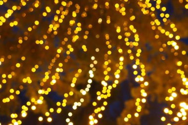 Bokeh röfleleri. Karanlıkta sarı ve altın rengi yanıp sönüyor. Şenlik arka planı. Bulanık defocus. Şehir sokaklarının dekorasyonu. Bir sürü sarı top. Birçok sarı, beyaz ve turuncu daireler