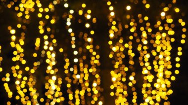 Bokeh röfleleri. Karanlıkta sarı ve altın rengi yanıp sönüyor. Şenlik arka planı. Bulanık defocus. Şehir sokaklarının dekorasyonu. Bir sürü sarı top. Birçok sarı, beyaz ve turuncu daireler