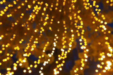 Bokeh röfleleri. Karanlıkta sarı ve altın rengi yanıp sönüyor. Şenlik arka planı. Bulanık defocus. Şehir sokaklarının dekorasyonu. Bir sürü sarı top. Birçok sarı, beyaz ve turuncu daireler