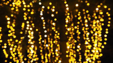Bokeh röfleleri. Karanlıkta sarı ve altın rengi yanıp sönüyor. Şenlik arka planı. Bulanık defocus. Şehir sokaklarının dekorasyonu. Bir sürü sarı top. Birçok sarı, beyaz ve turuncu daireler