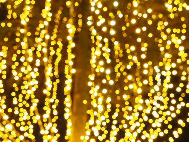 Bokeh röfleleri. Karanlıkta sarı ve altın rengi yanıp sönüyor. Şenlik arka planı. Bulanık defocus. Şehir sokaklarının dekorasyonu. Bir sürü sarı top. Birçok sarı, beyaz ve turuncu daireler