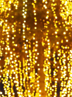 Bokeh röfleleri. Karanlıkta sarı ve altın rengi yanıp sönüyor. Şenlik arka planı. Bulanık defocus. Şehir sokaklarının dekorasyonu. Bir sürü sarı top. Birçok sarı, beyaz ve turuncu daireler