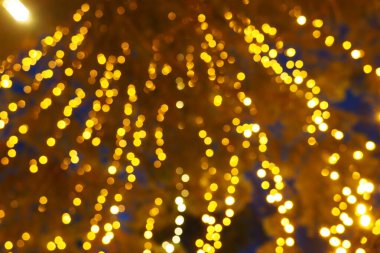 Bokeh röfleleri. Karanlıkta sarı ve altın rengi yanıp sönüyor. Şenlik arka planı. Bulanık defocus. Şehir sokaklarının dekorasyonu. Bir sürü sarı top. Birçok sarı, beyaz ve turuncu daireler