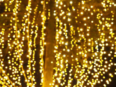 Bokeh röfleleri. Karanlıkta sarı ve altın rengi yanıp sönüyor. Şenlik arka planı. Bulanık defocus. Şehir sokaklarının dekorasyonu. Bir sürü sarı top. Birçok sarı, beyaz ve turuncu daireler