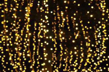 Bokeh röfleleri. Karanlıkta sarı ve altın rengi yanıp sönüyor. Şenlik arka planı. Bulanık defocus. Şehir sokaklarının dekorasyonu. Bir sürü sarı top. Birçok sarı, beyaz ve turuncu daireler