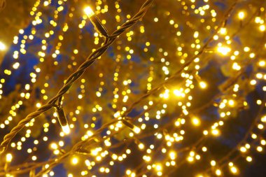 Bokeh röfleleri. Karanlıkta sarı ve altın rengi yanıp sönüyor. Şenlik arka planı. Bulanık defocus. Şehir sokaklarının dekorasyonu. Bir sürü sarı top. Birçok sarı, beyaz ve turuncu daireler