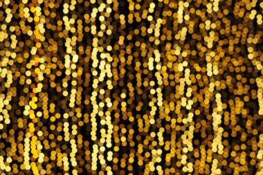 Bokeh röfleleri. Karanlıkta sarı ve altın rengi yanıp sönüyor. Şenlik arka planı. Bulanık defocus. Şehir sokaklarının dekorasyonu. Bir sürü sarı top. Birçok sarı, beyaz ve turuncu daireler