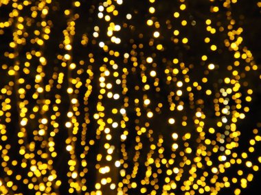 Bokeh röfleleri. Karanlıkta sarı ve altın rengi yanıp sönüyor. Şenlik arka planı. Bulanık defocus. Şehir sokaklarının dekorasyonu. Bir sürü sarı top. Birçok sarı, beyaz ve turuncu daireler