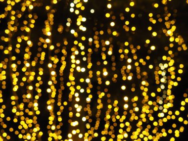 Bokeh röfleleri. Karanlıkta sarı ve altın rengi yanıp sönüyor. Şenlik arka planı. Bulanık defocus. Şehir sokaklarının dekorasyonu. Bir sürü sarı top. Birçok sarı, beyaz ve turuncu daireler