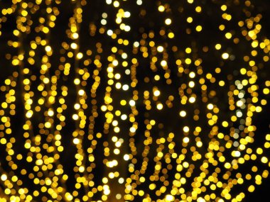 Bokeh röfleleri. Karanlıkta sarı ve altın rengi yanıp sönüyor. Şenlik arka planı. Bulanık defocus. Şehir sokaklarının dekorasyonu. Bir sürü sarı top. Birçok sarı, beyaz ve turuncu daireler