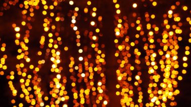 Bokeh röfleleri. Karanlıkta sarı ve altın rengi yanıp sönüyor. Şenlik arka planı. Bulanık defocus. Şehir sokaklarının dekorasyonu. Bir sürü sarı top. Birçok sarı, beyaz ve turuncu daireler
