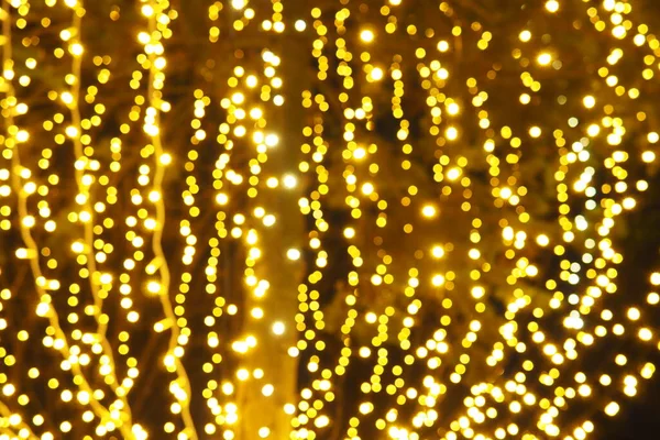 Bokeh röfleleri. Karanlıkta sarı ve altın rengi yanıp sönüyor. Şenlik arka planı. Bulanık defocus. Şehir sokaklarının dekorasyonu. Bir sürü sarı top. Birçok sarı, beyaz ve turuncu daireler